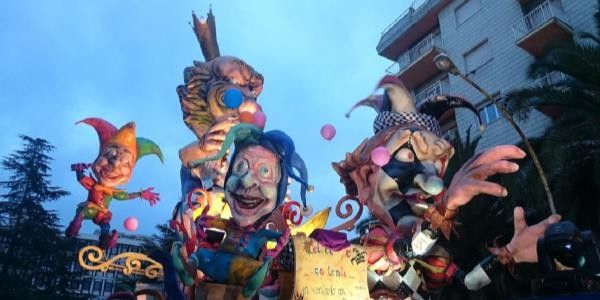 Carri allegorici colorati del Carnevale, con figure di clown e giocolieri, che animano le strade in un'atmosfera festosa e vivace
